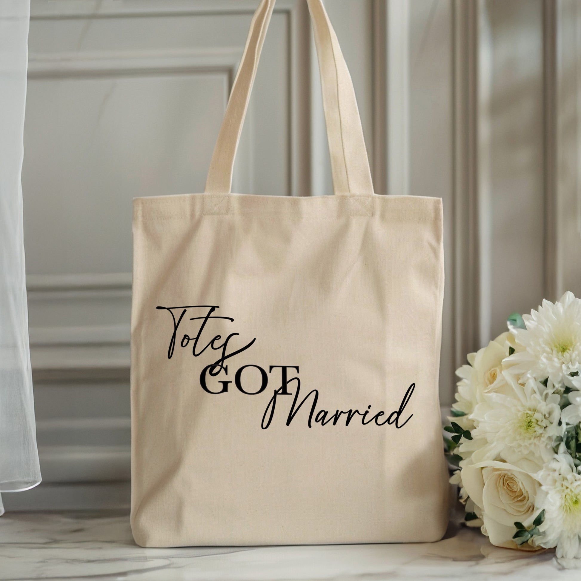 Beige tote bag with 'Totes Got Married' text next to white flowers