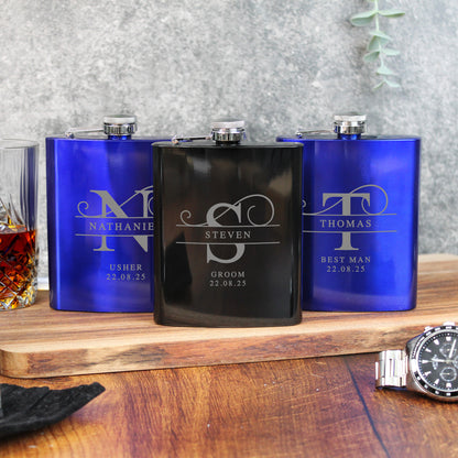 Three personalized flasks on a wooden surface with a glass of whiskey and a watch.