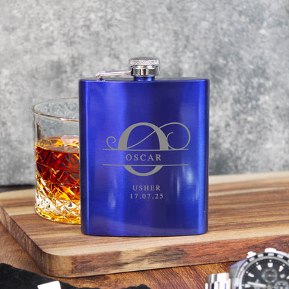 Blue flask with 'Oscar Usher' engraving next to a glass of whiskey on a wooden surface.