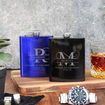 Two personalized flasks, one blue and one black, on a wooden surface with a glass of whiskey.