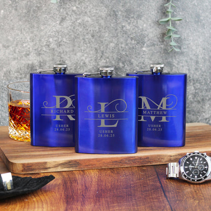 Three blue flasks with engraved names on a wooden surface with a glass of whiskey.