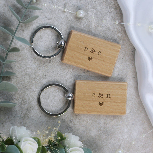 Two wooden keychains with engraved initials on a textured surface with flowers and leaves.