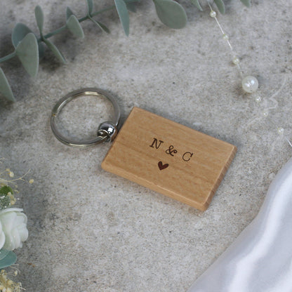 Wooden keychain with 'N & C' engraving on a concrete surface with greenery.