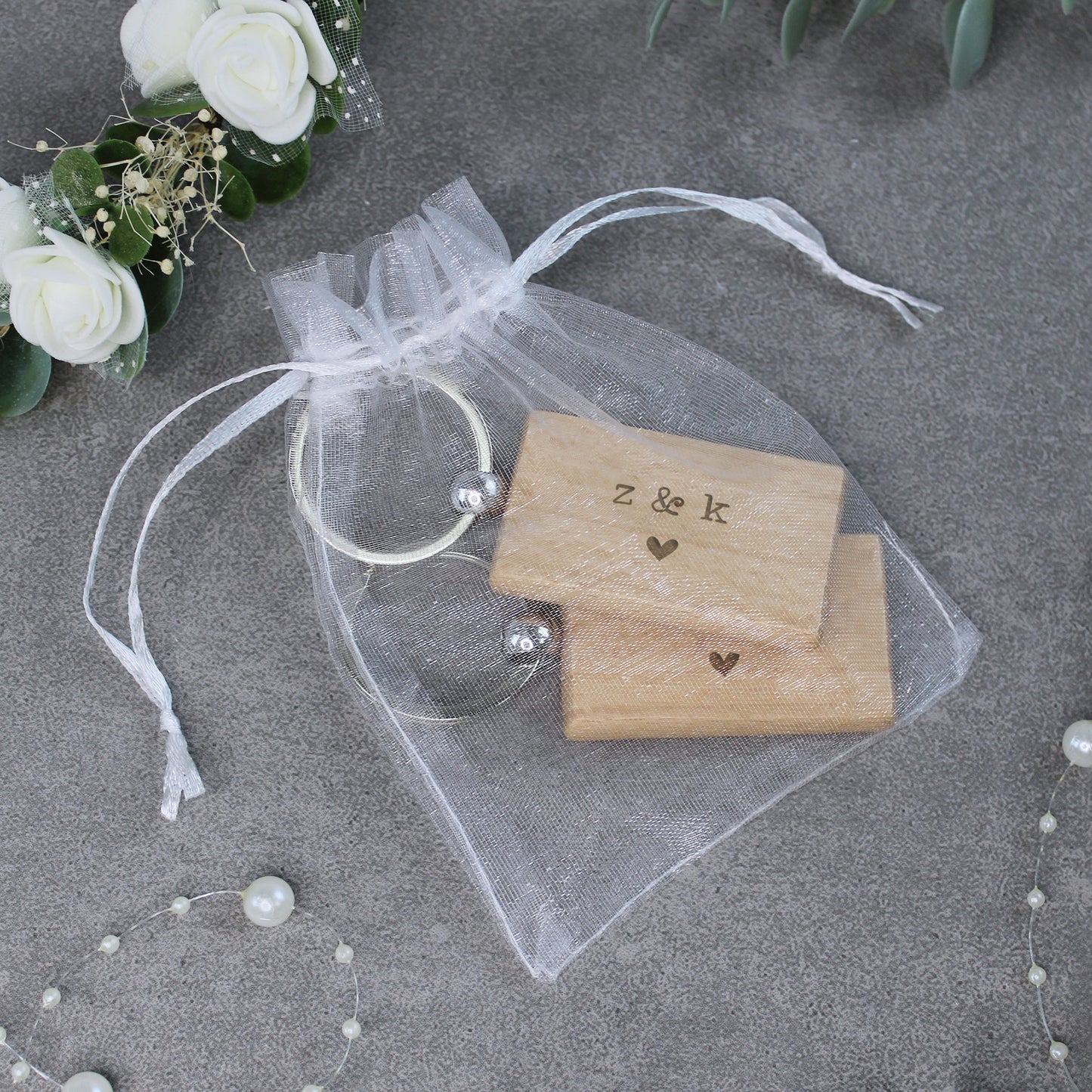 Wooden stamp set with 'z & k' and heart designs on a sheer white bag with flowers and pearls in the background.