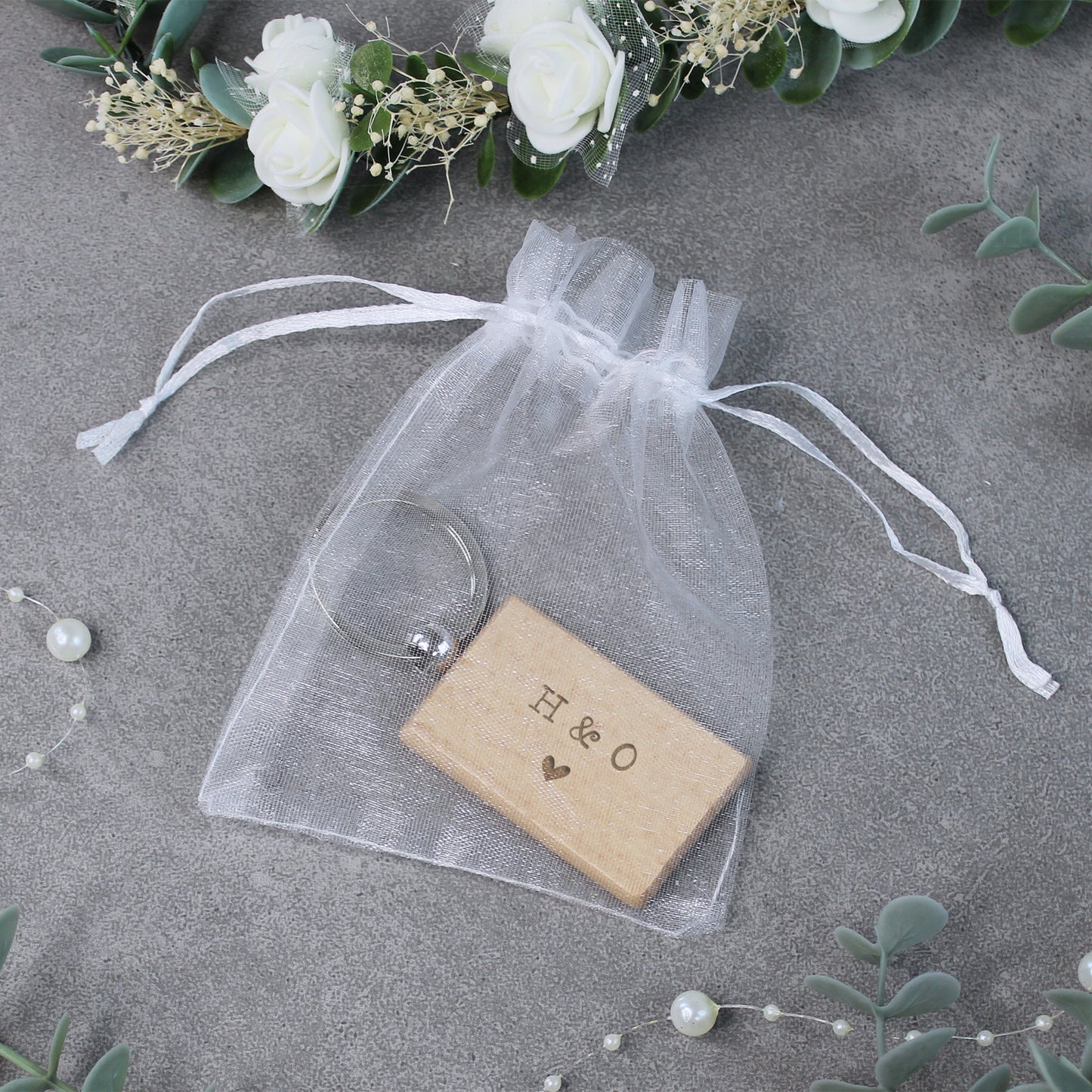 Wooden block with 'H & O' engraving in a clear drawstring bag on a gray surface with floral decorations.