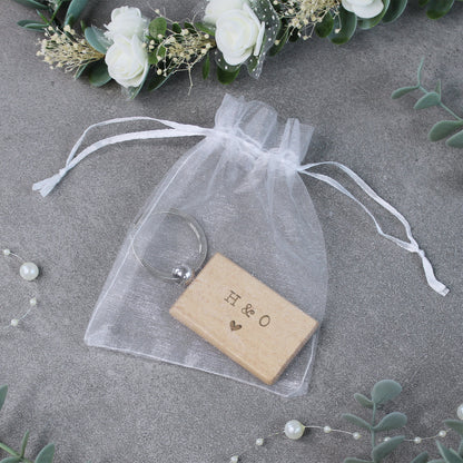 Wooden block with 'H & O' engraving in a clear drawstring bag on a gray surface with floral decorations.