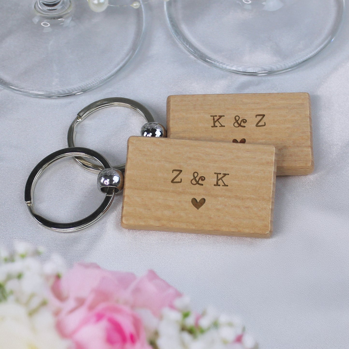 Wooden keychains with 'K & Z' and 'Z & K' engraved, placed on a white surface with flowers.