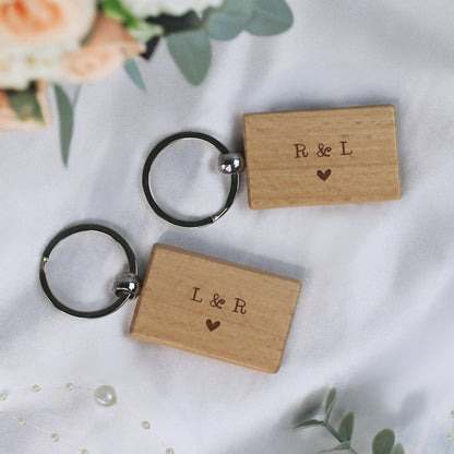 Two wooden keychains with 'R & L' and 'L & R' engraved on them, placed on a white surface with floral elements.
