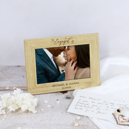Wooden photo frame with engraved text displaying a couple's engagement photo on a light surface.