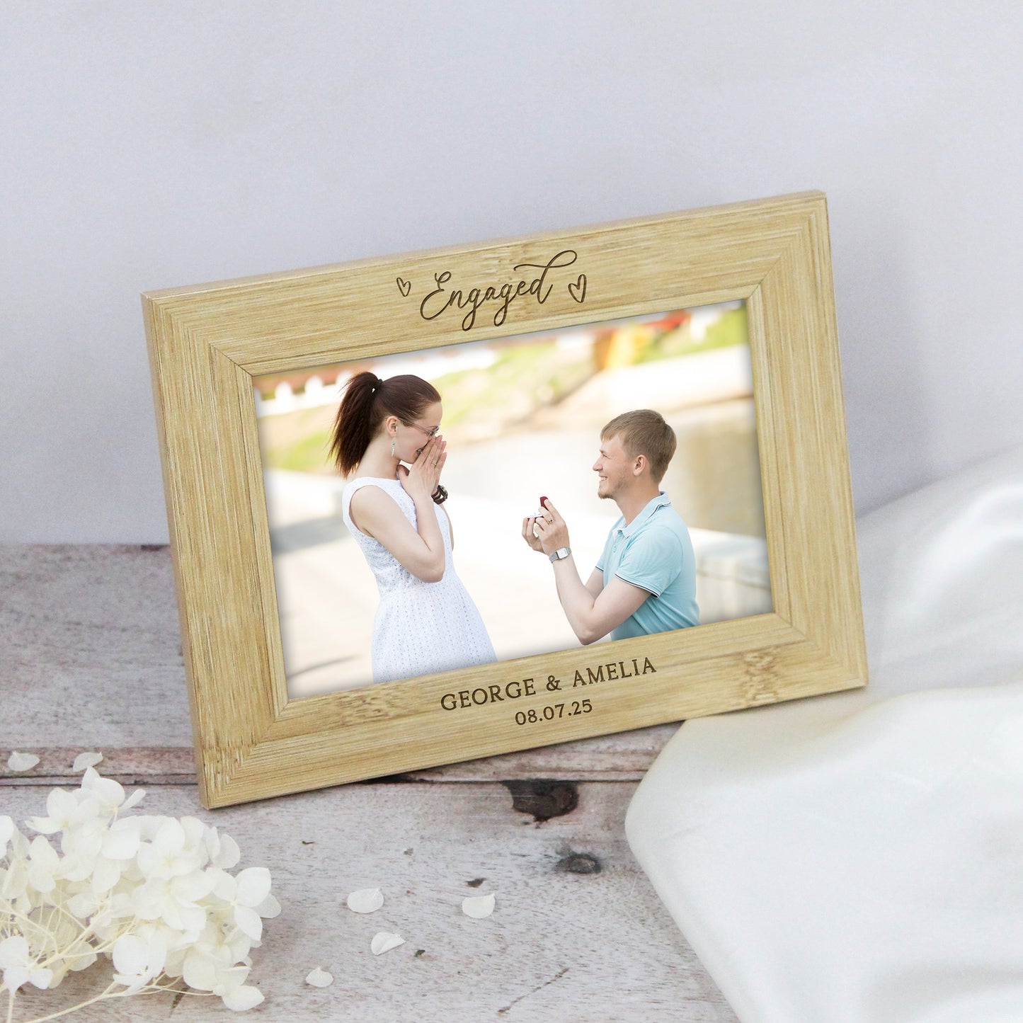 Wooden photo frame with engraved text, displaying a couple on a wooden surface with flowers.