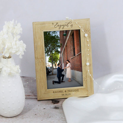 Wooden photo frame with engraved text displaying a couple getting engaged, placed on a surface with decorative elements.