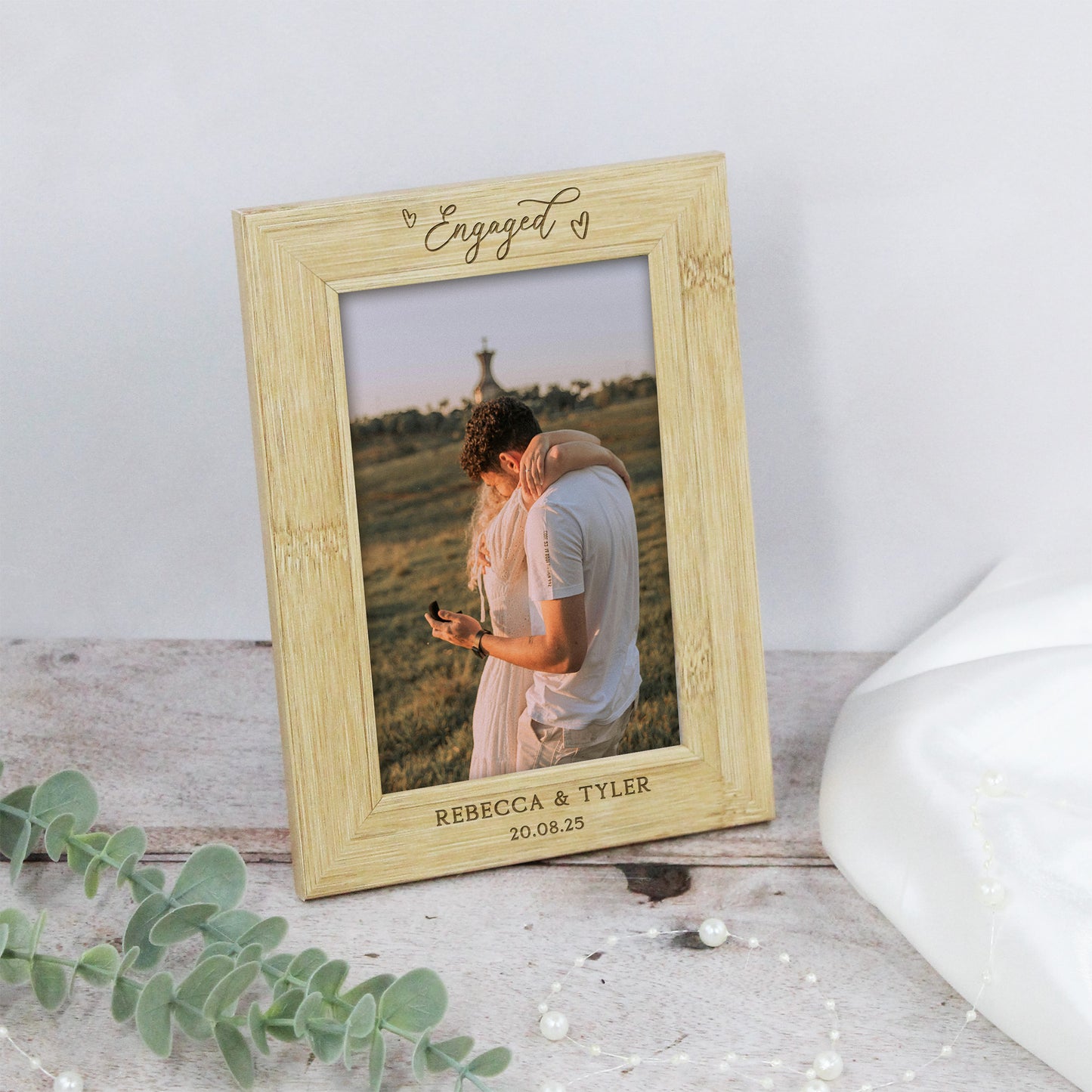 Wooden photo frame with engraved text and a couple's picture inside, on a light wooden surface.