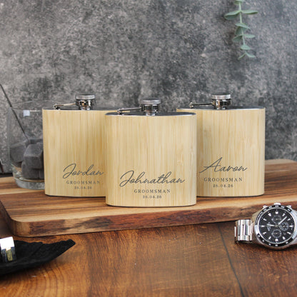Three wooden flasks with engraved names on a wooden surface with a watch in the foreground.