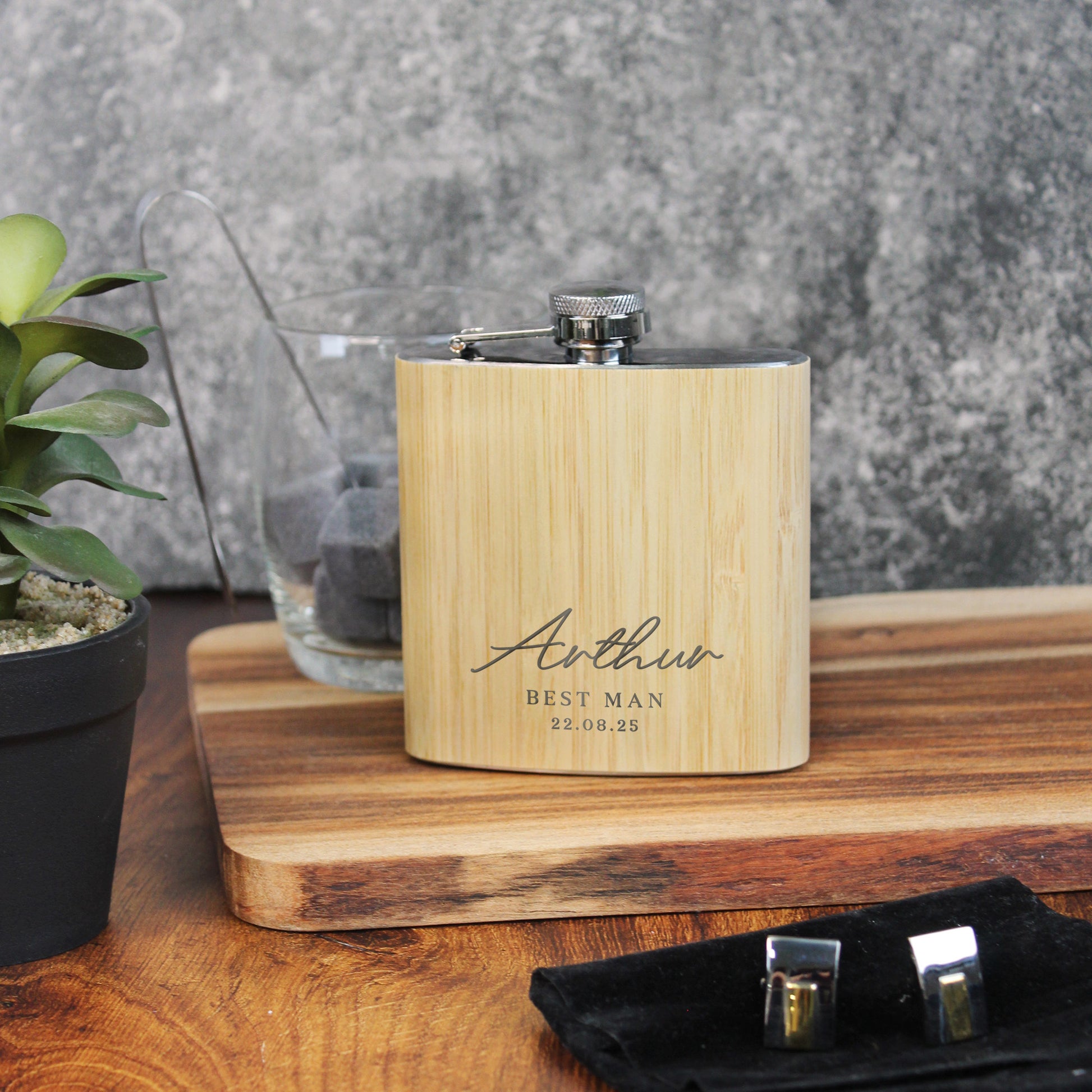 Wooden flask with engraved text on a wooden surface with a plant and glass bowl in the background.